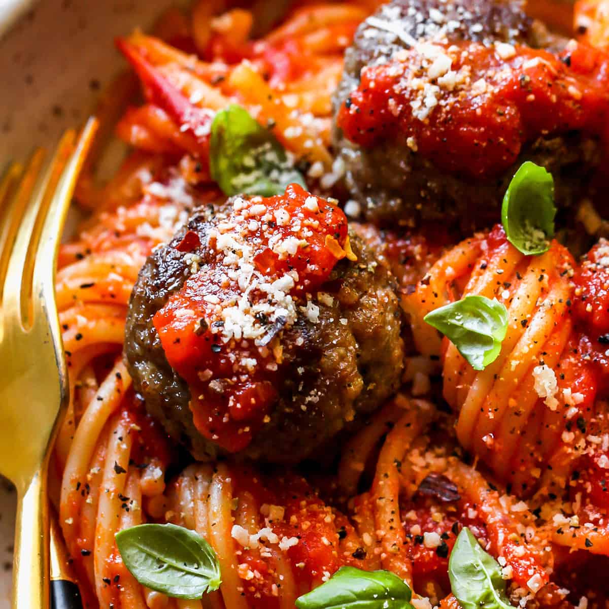 up close view of homemade meatballs over pasta in marinara sauce garnished with basil