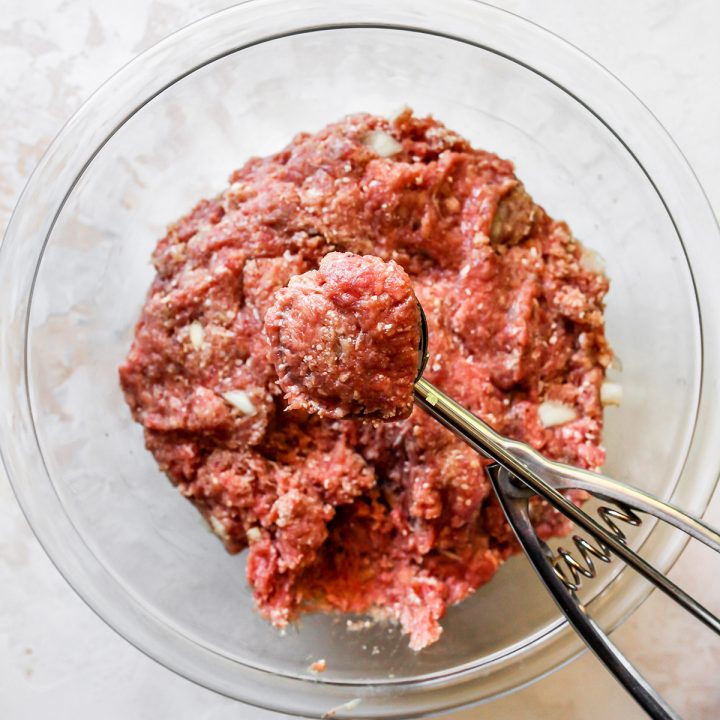 a 1 tablespoon scoop measuring out a portion of the meatball recipe mixture 