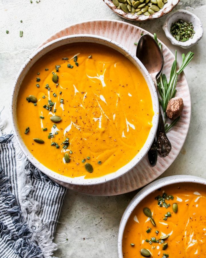 two bowls of Sweet Potato Soup garnished with rosemary, cream and seeds. 