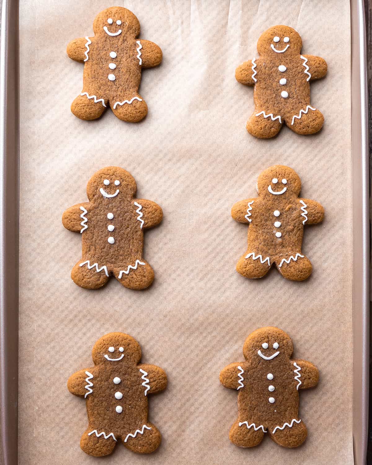 6 gingerbread men cookies on a baking sheet decorated with faces and buttons