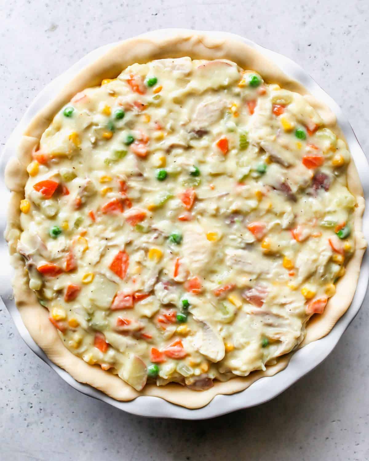 assembling turkey pot pie recipe - bottom crust and filling in a white pie dish on a gray surface