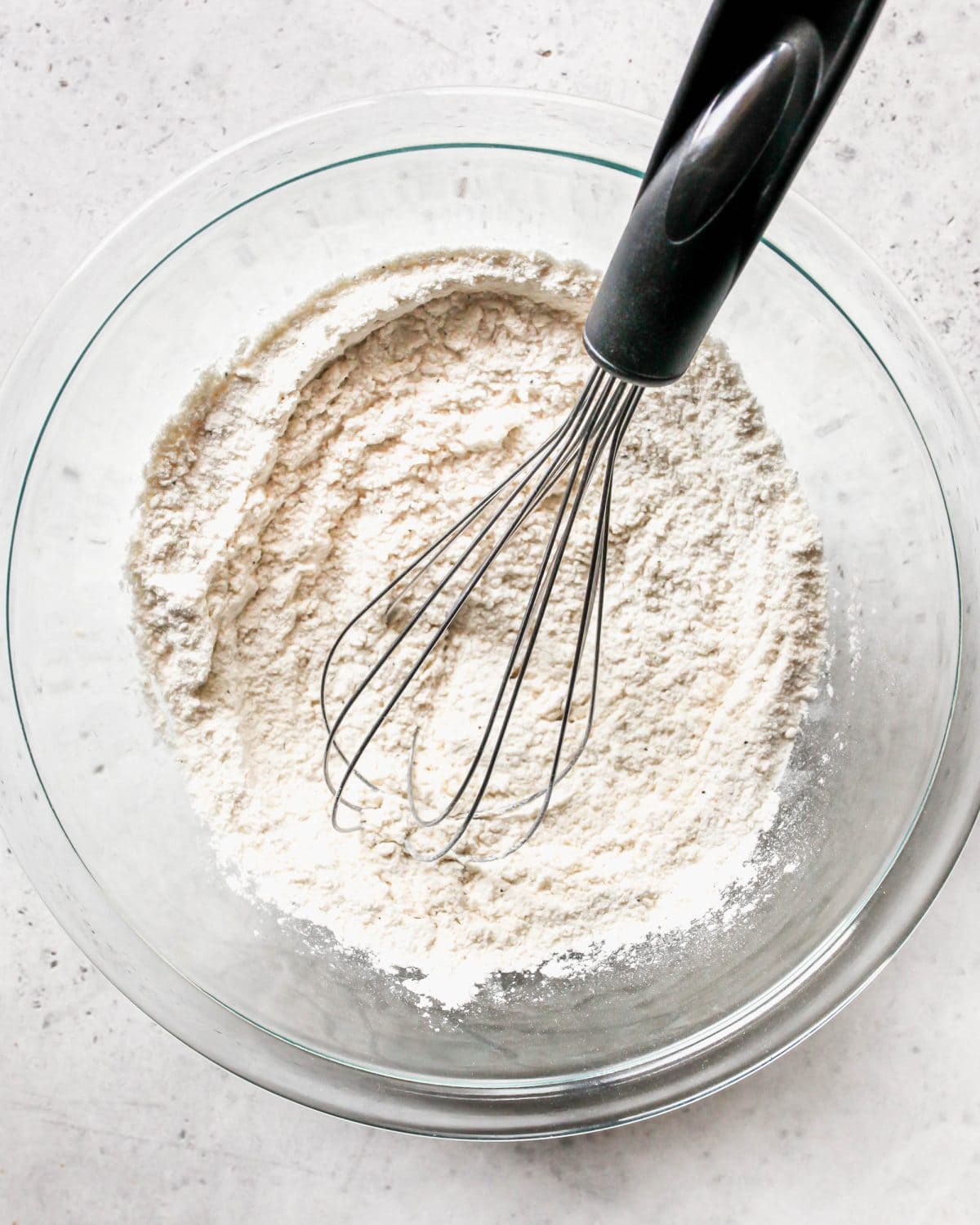 making turkey pot pie recipe - flour, onion powder, garlic powder, salt and pepper in a glass bowl with a wire whisk on a gray surface