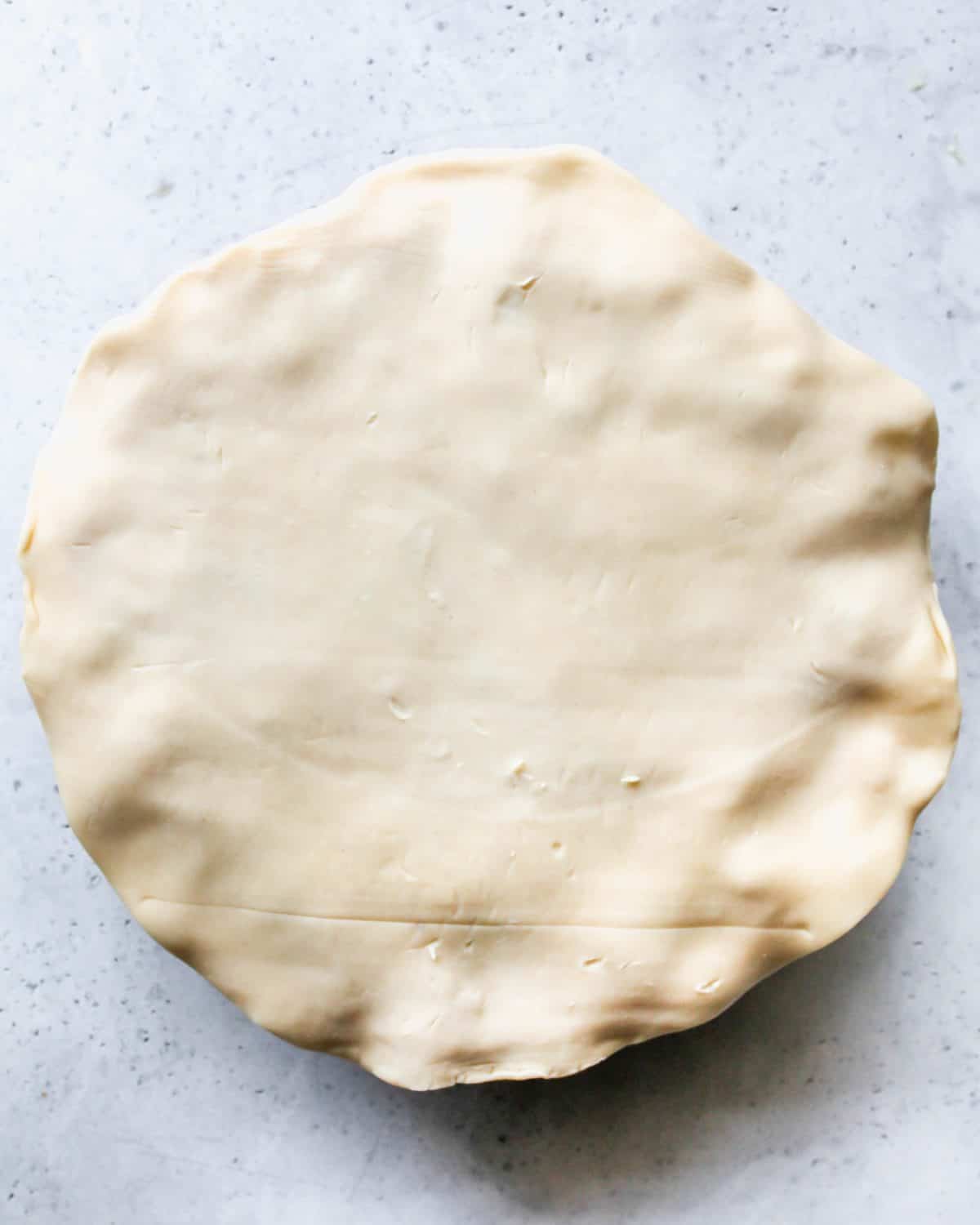 assembling turkey pot pie recipe - top crust put over the bottom crust and filling in a white pie dish on a gray surface before shaping.