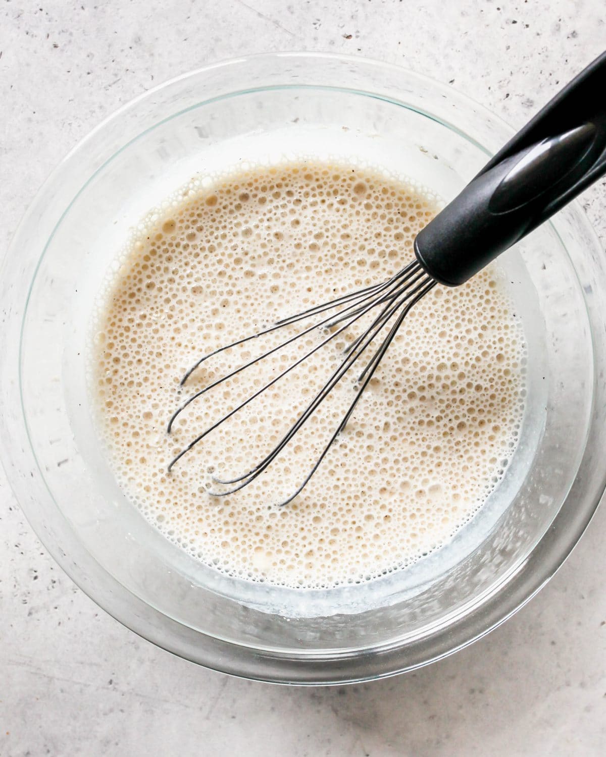 making turkey pot pie recipe - flour, onion powder, garlic powder, salt and pepper and milk in a glass bowl with a wire whisk on a gray surface