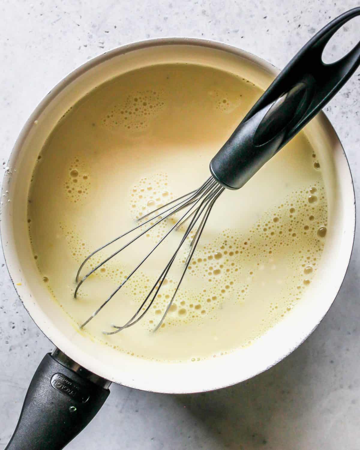 making turkey pot pie recipe - sauce ingredients whisked together in a white saucepan with a metal whisk with a black handle