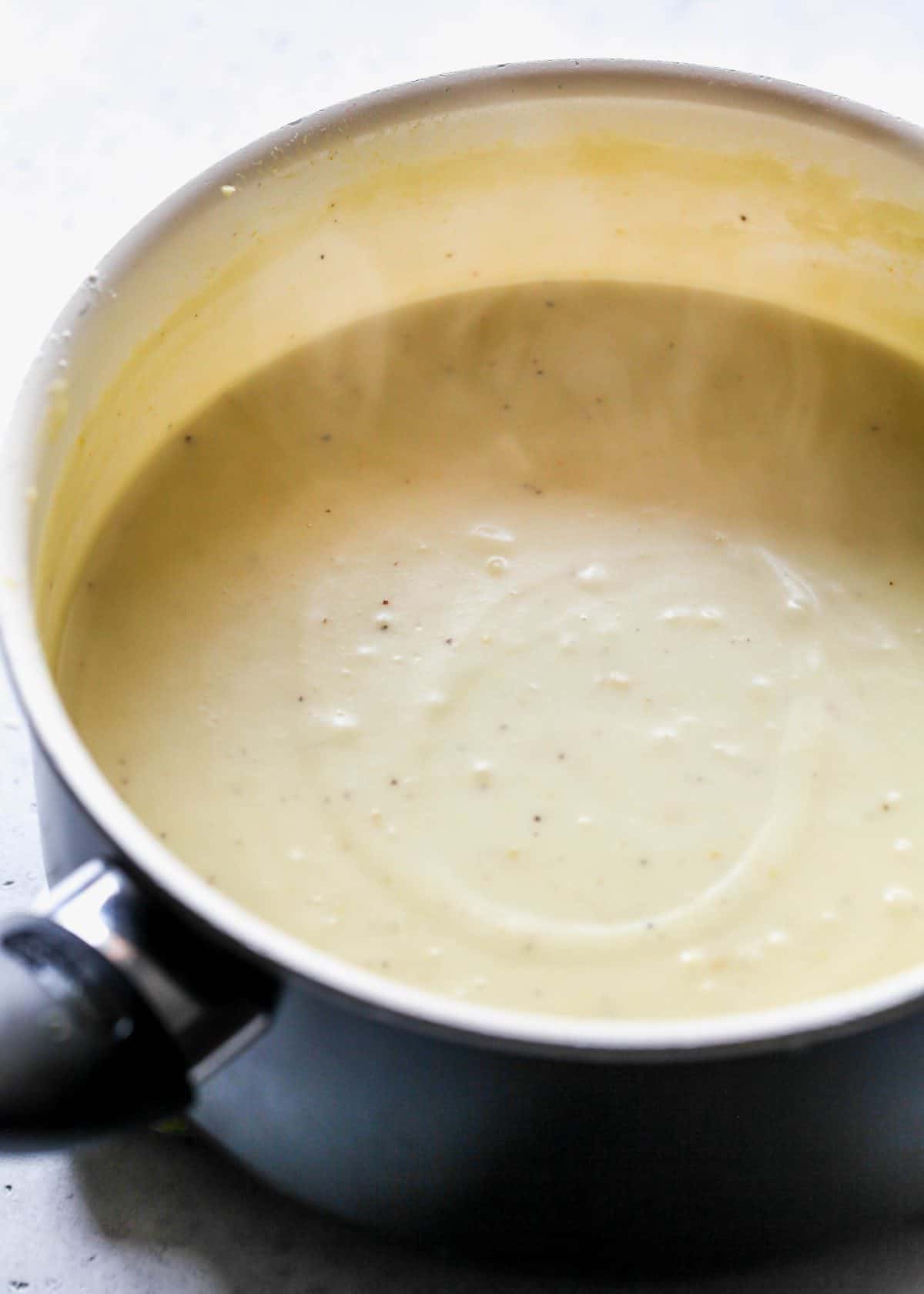 making turkey pot pie recipe - thickened sauce in a white saucepan. The important thing here is the slightly thickened texture of the sauce which is visible in this photo.