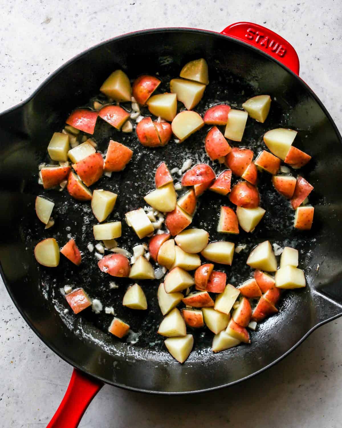 making turkey pot pie recipe - red potatoes, minced garlic and butter cooking in a large cast iron skillet with a black bottom and red exterior.