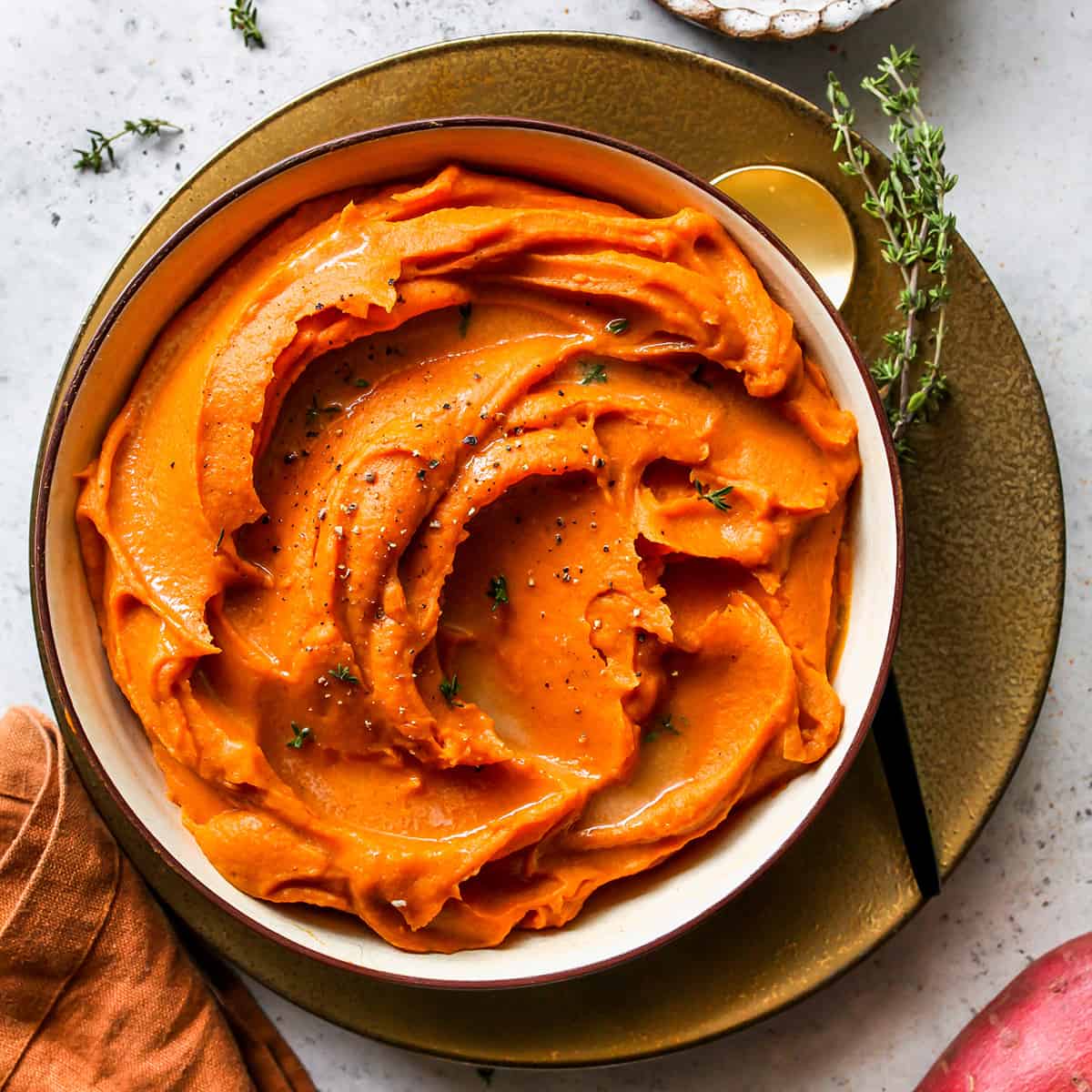 Mashed Sweet Potatoes in a bowl garnished with melted butter and chopped thyme