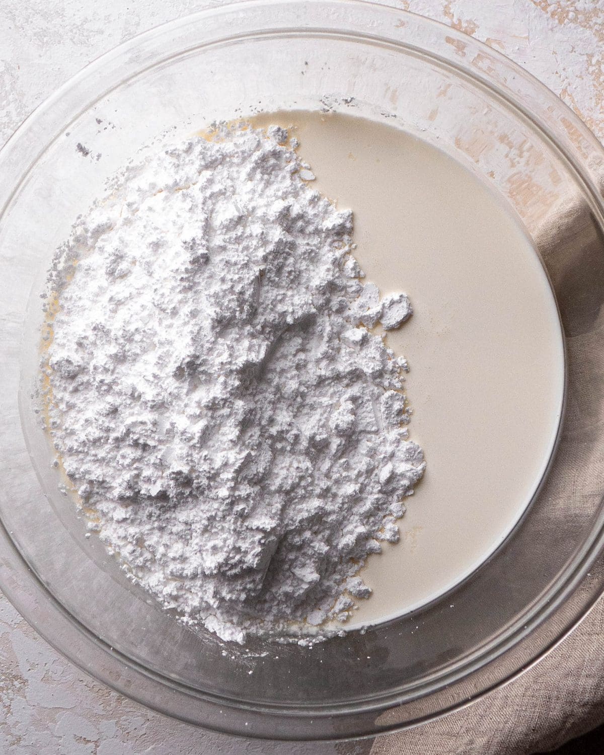 making Oreo pie recipe - heavy whipping cream and powdered sugar in a glass mixing bowl on a gray surface before beating