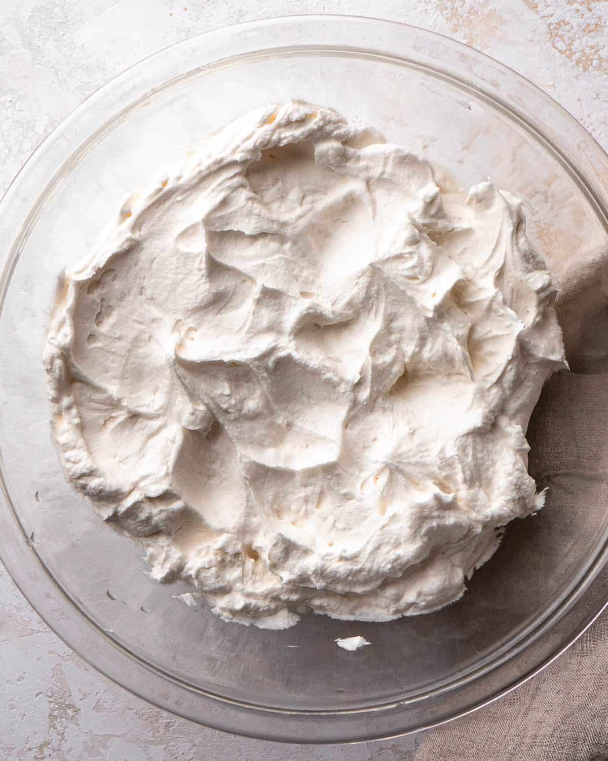 making Oreo pie recipe - Whipped cream in a glass mixing bowl on a gray surface