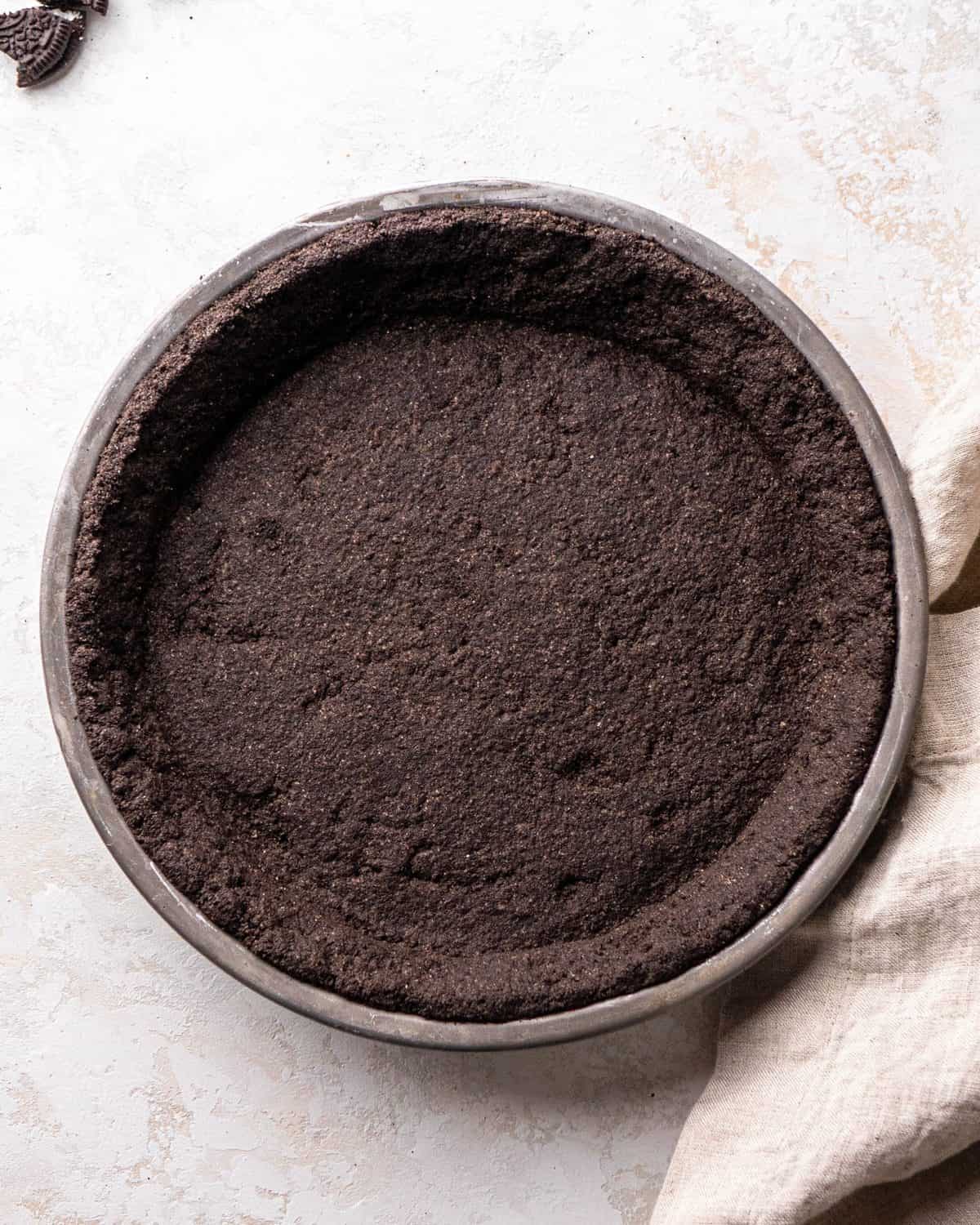 making Oreo pie recipe - baked Oreo pie crust in a metal pie dish on a gray surface