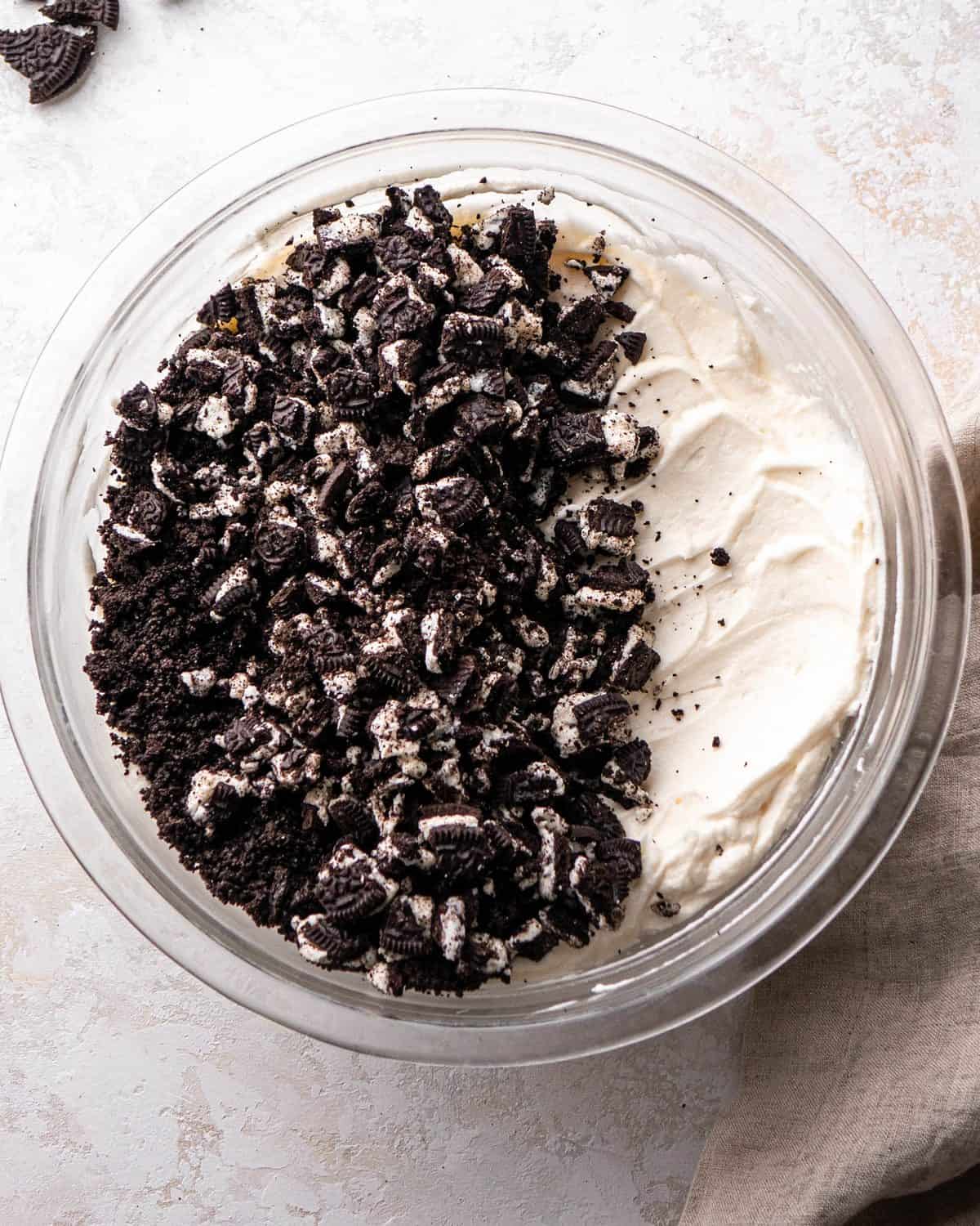 making Oreo pie recipe - Oreo pieces and crumbs added to the filling mixture in a glass bowl before mixing
