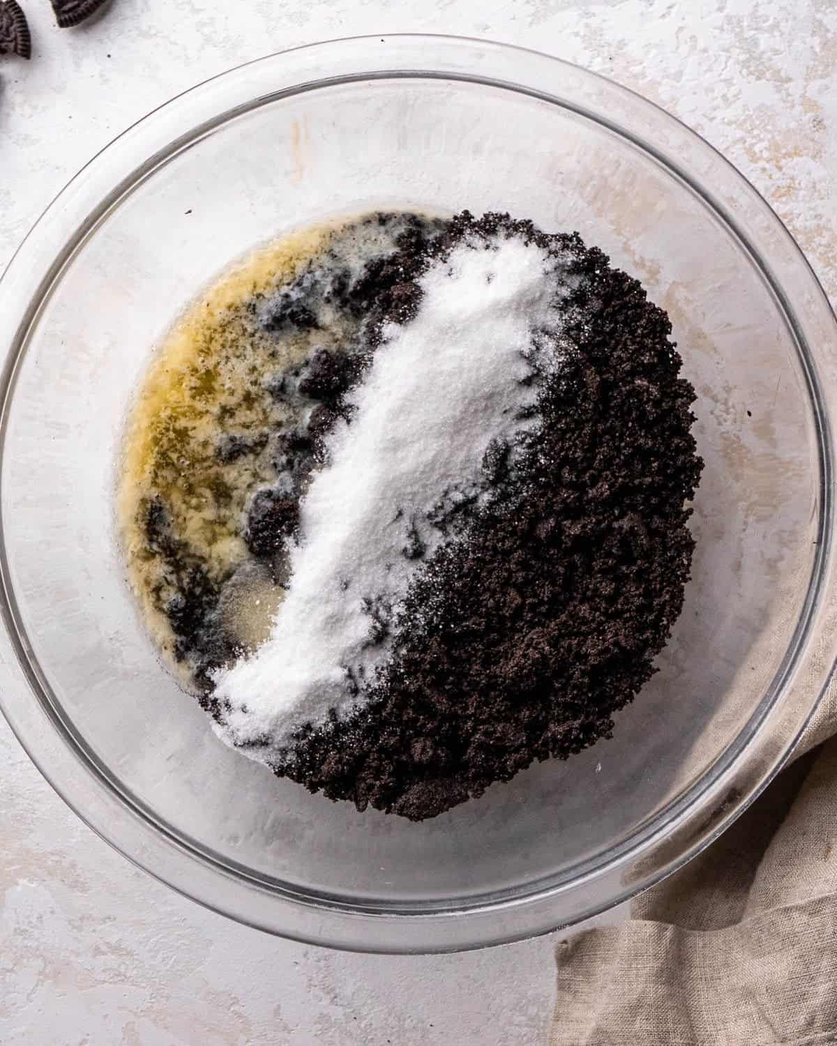 making oreo pie recipe - Oreo crumbs, butter and sugar in a glass bowl on a gray surface before mixing