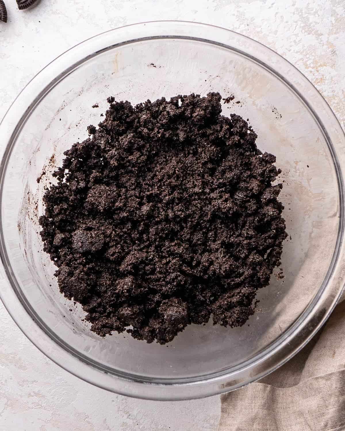 making oreo pie recipe - oreo crust ingredients mixed together in a glass bowl on a gray surface