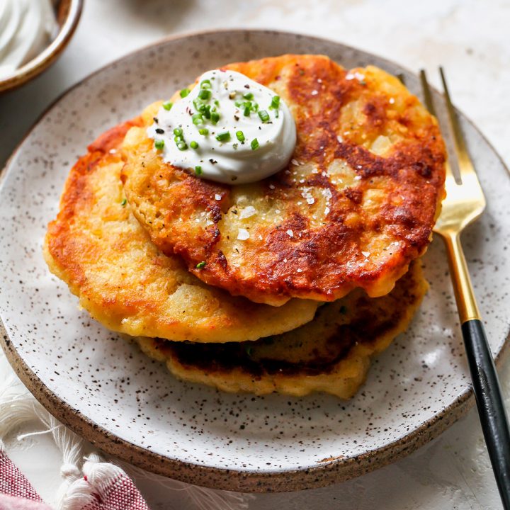 a stack of 3 Potato Pancakes garnished with sour cream and chives.