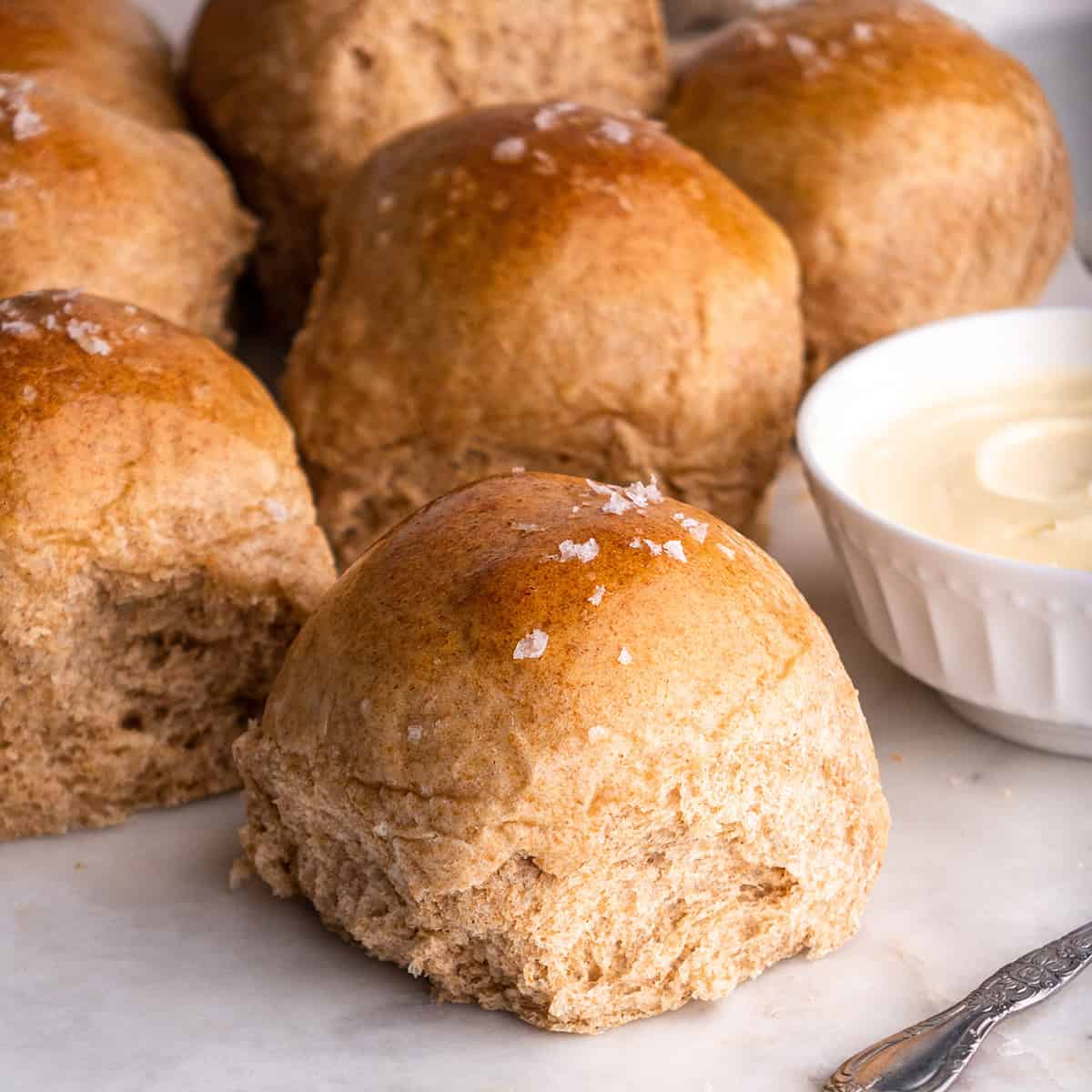 front view of six Whole Wheat Dinner Rolls with butter and sea salt on top