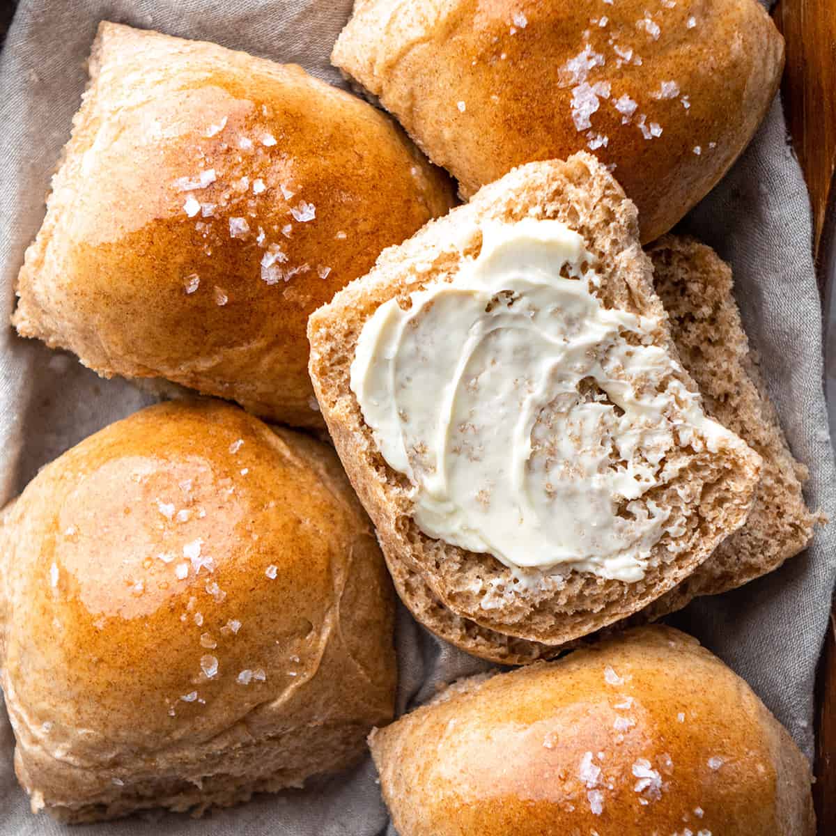 a Whole Wheat Roll cut in half with butter spread over it and four other rolls around it.