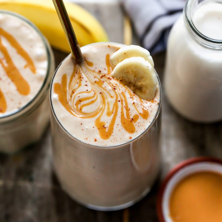 glass of Banana Peanut Butter Smoothie topped with cinnamon, peanut butter swirl and two slices of banana