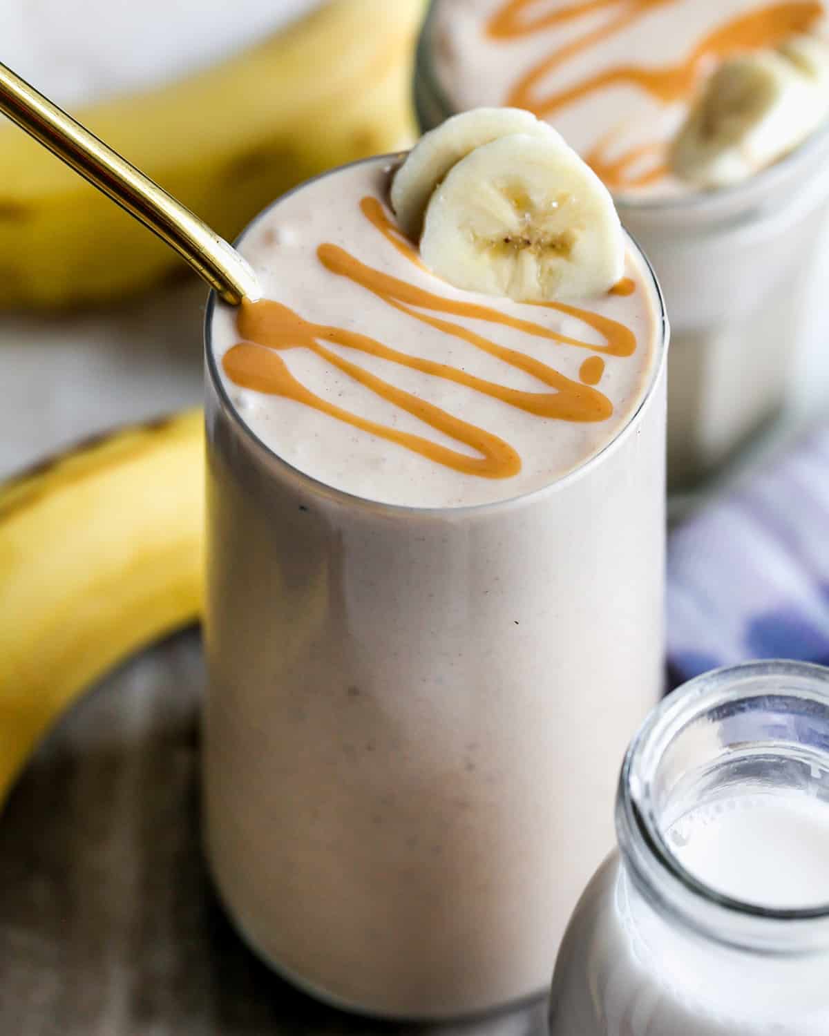 glass of Banana Peanut Butter Smoothie topped with a peanut butter drizzle and two slices of banana