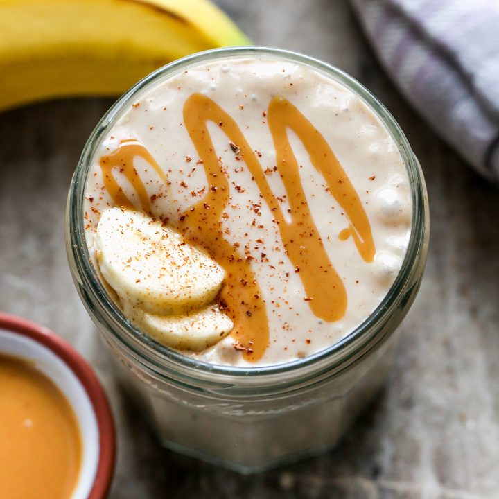 glass of Banana Peanut Butter Smoothie topped with cinnamon, peanut butter drizzle and two slices of banana