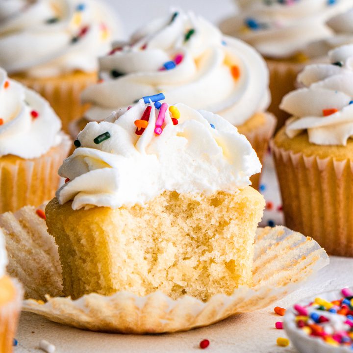 a Vanilla Cupcake topped with with frosting and sprinkles with a bite taken out of it