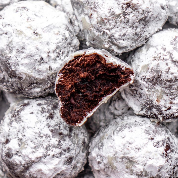 overhead photo of Chocolate Snowball Cookies, one has a bite taken out of it so you can see the inside of the cookie