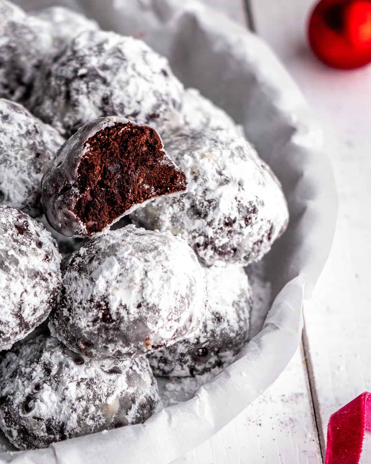 Chocolate Snowball Cookies in a serving dish, one has a bite taken out of it so you can see the inside