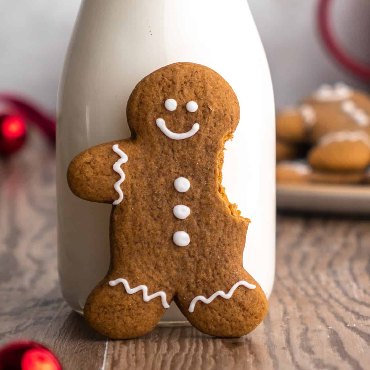 a gingerbread man cookie standing up leaning against a bottle of milk with his arm bitten off