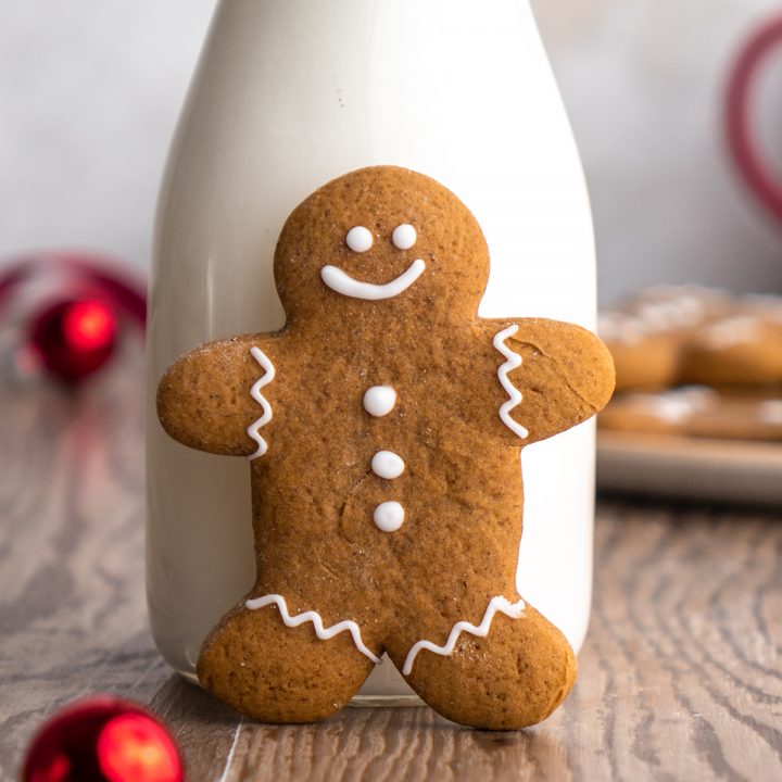 a gingerbread man cookie standing up leaning against a bottle of milk