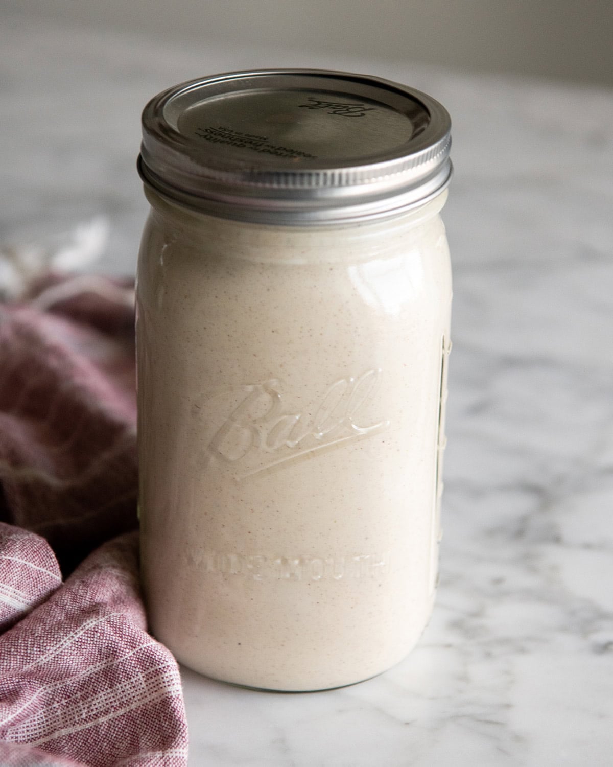 homemade eggnog recipe in a glass jar with a lid to be chilled, there's a red towel on the left side