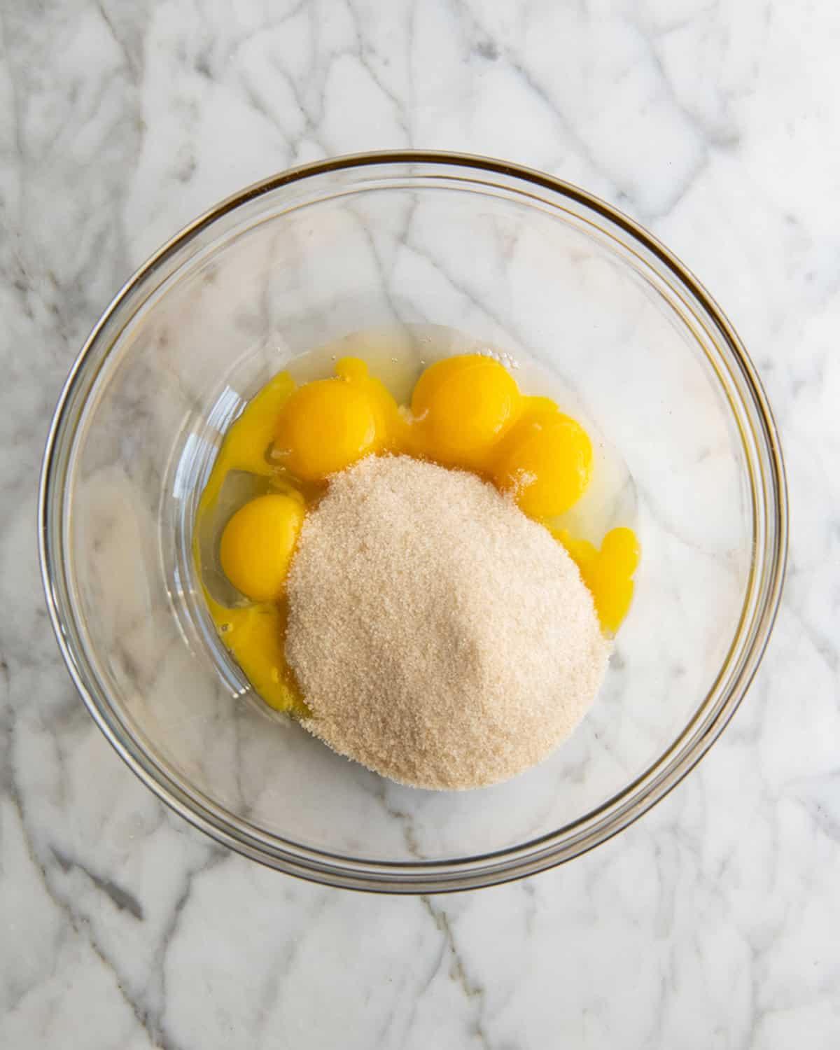 how to make eggnog recipe - 6 egg yolks and granulated sugar in a glass mixing bowl on a marble surface before beating