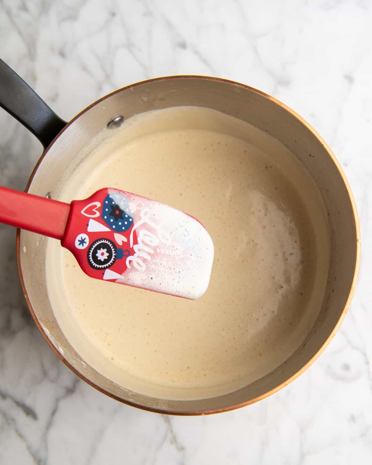 how to make eggnog recipe - a spatula with the custard mixture coating it being held over the copper pot with the rest of the homemade eggnog mixture in it