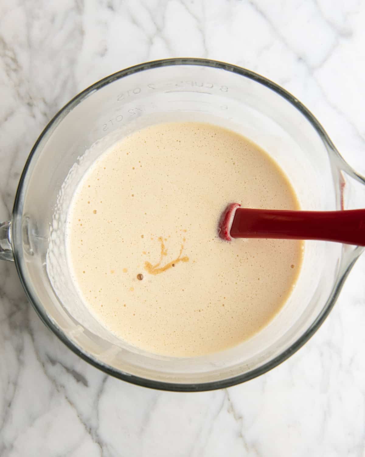 how to make eggnog recipe - vanilla added to the eggnog mixture in a glass batter bowl with a red spatula.