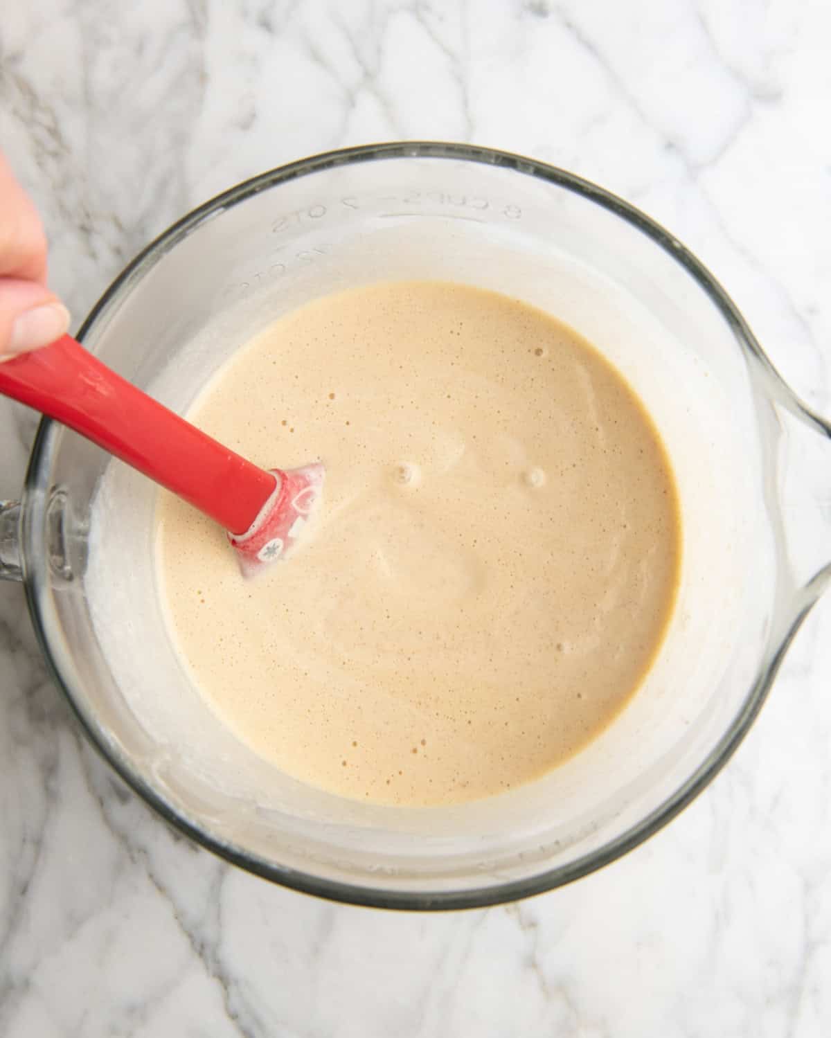 how to make eggnog recipe - final mixture in a glass batter bowl with a red spatula on a marble suraface