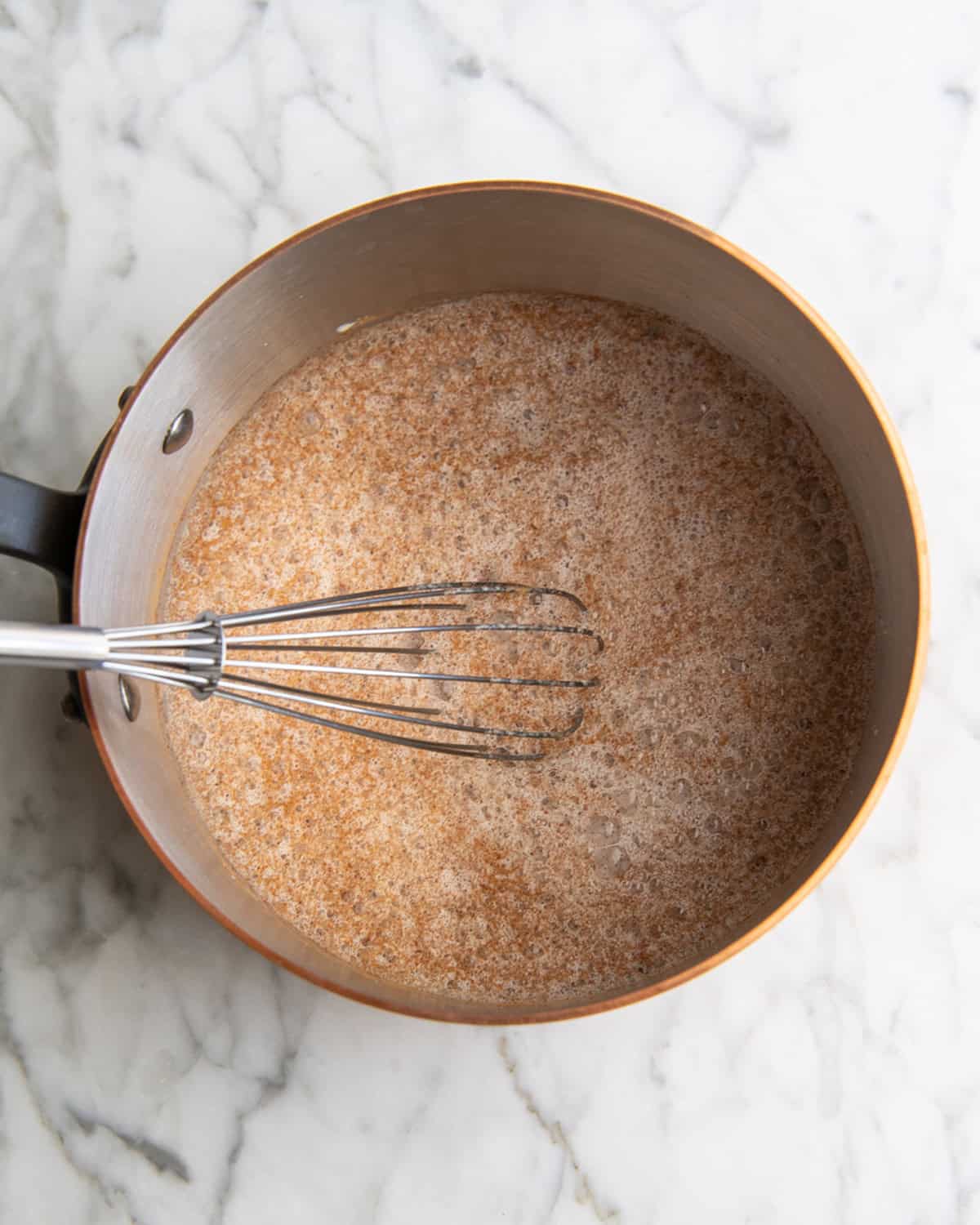 how to make eggnog recipe - cinnamon and nutmeg whisked in to milk with a metal wire whisk in a copper saucepan before mixing