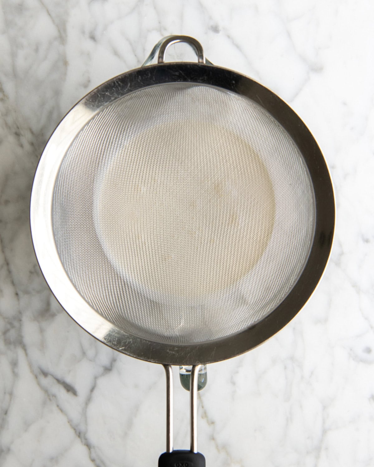 how to make eggnog recipe - a fine mesh metal strainer on top of a glass batter bowl with heavy cream in it