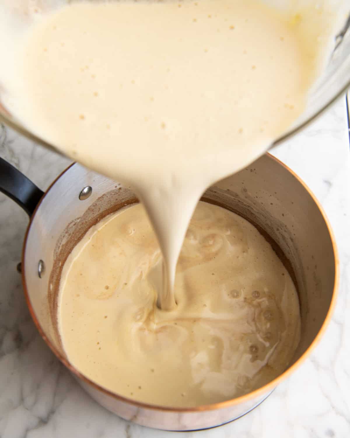how to make eggnog recipe - tempered egg and milk mixture being poured into the copper saucepan with milk in it