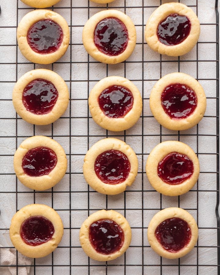 12 raspberry thumbprint cookies on a wire cooling rack