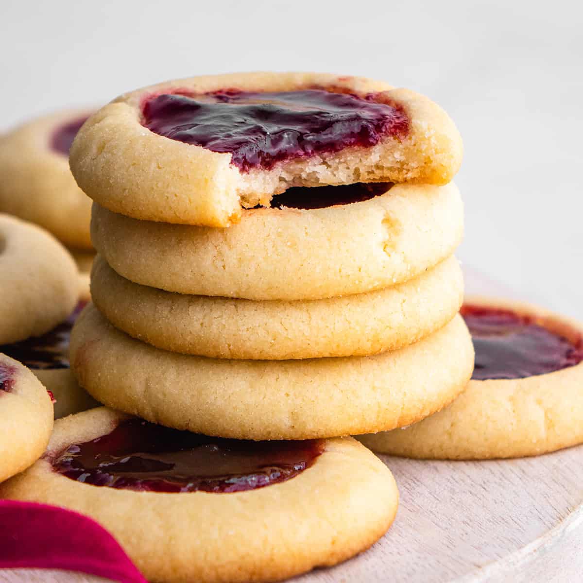 stack of four raspberry thumbprint cookies, the top one has a bite taken out of it