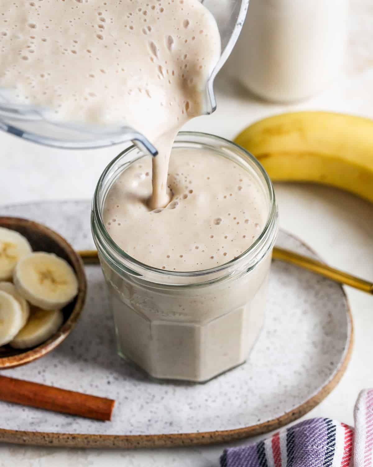 Banana smoothie being poured from the blending container into a glass 