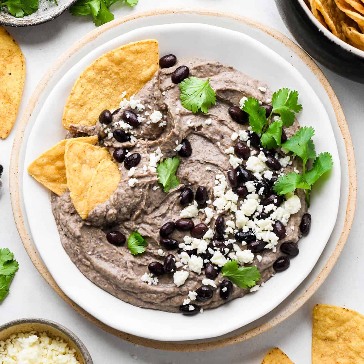 a bowl of Black Bean Dip garnished with cilantro. black beans, cheese and chips