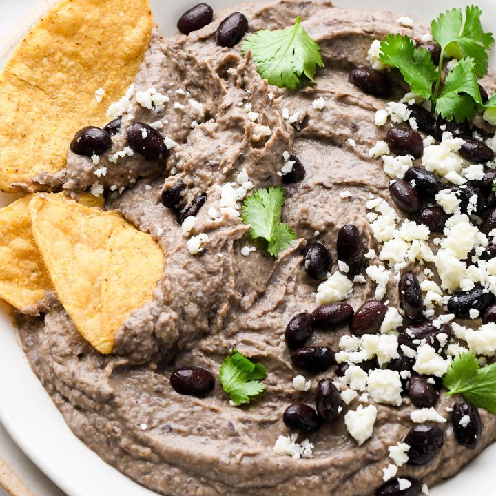 a bowl of Black Bean Dip garnished with cilantro. black beans, cheese and chips