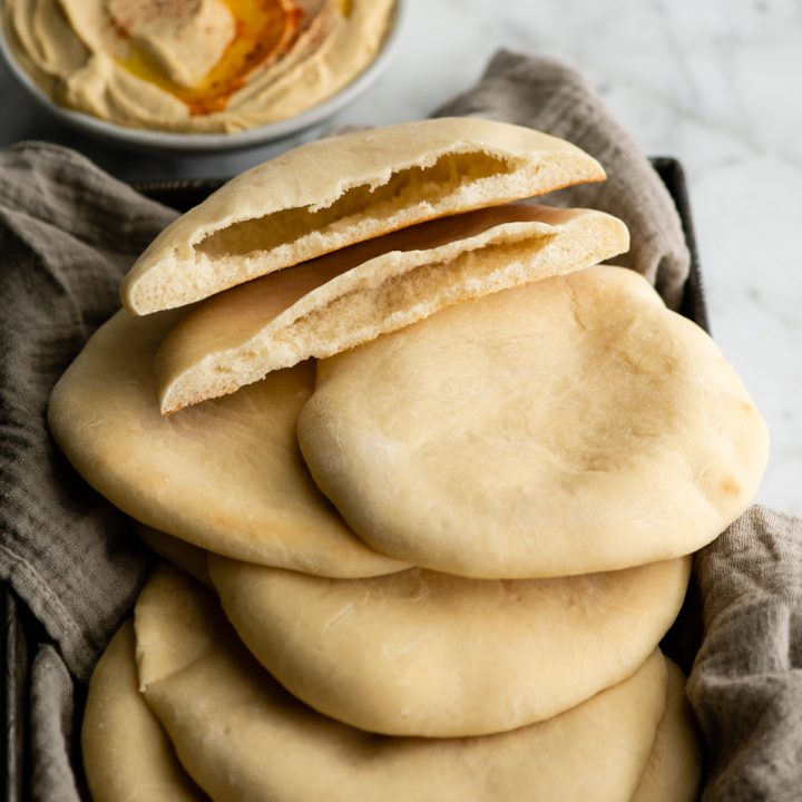 homemade Pita Bread  cut in half with the pocket inside showing on top of 5 other pita breads