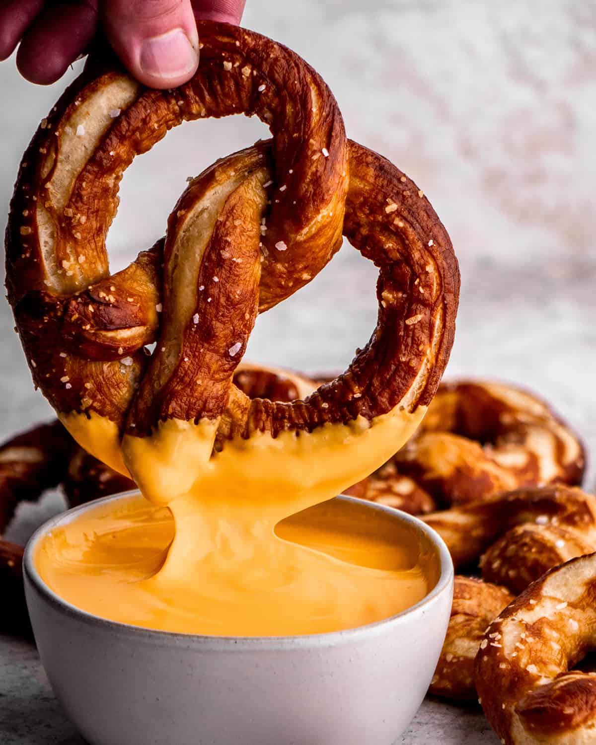 a homemade soft pretzel being dipped into cheese sauce