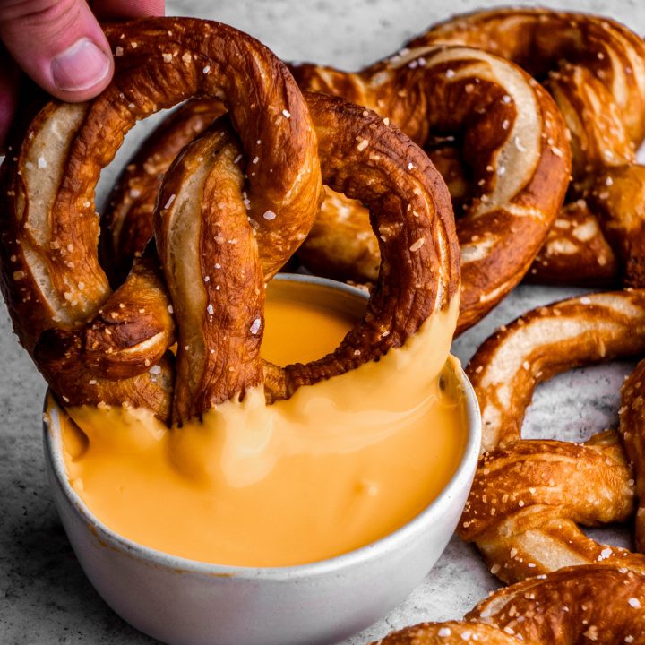 a homemade soft pretzel being dipped in cheese sauce