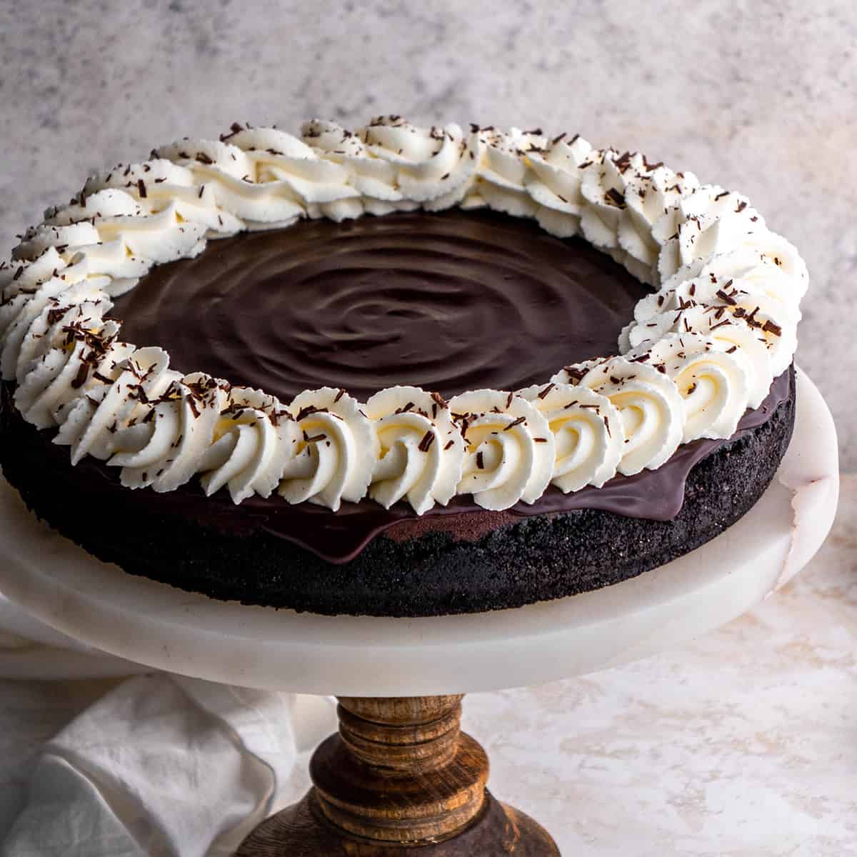 Chocolate Cheesecake on a cake plate topped with whipped cream and chocolate shavings 