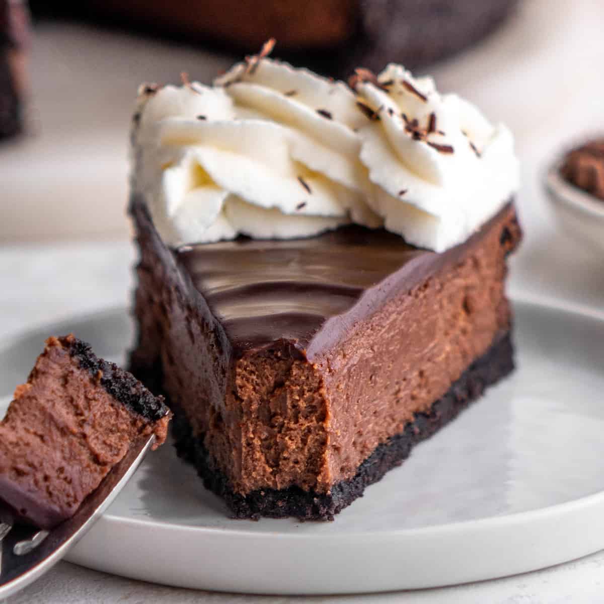 a slice of Chocolate Cheesecake on a plate with whipped cream on top and a bite taken out of it