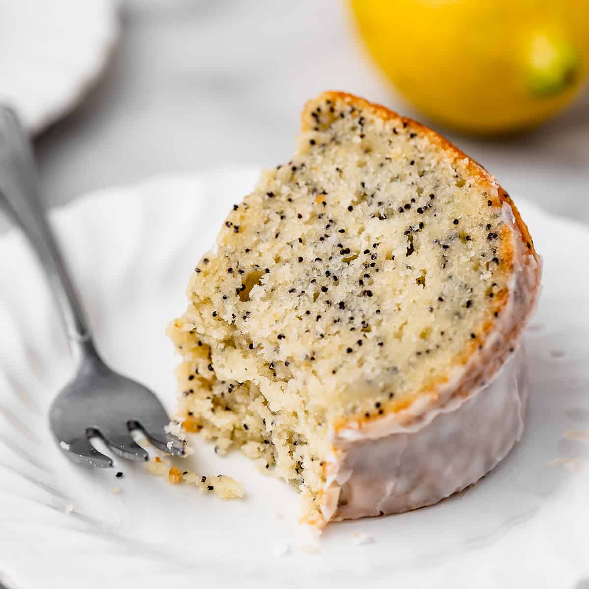 a slice of Lemon Poppy Seed Cake on a cake with a fork and a bite taken out of it