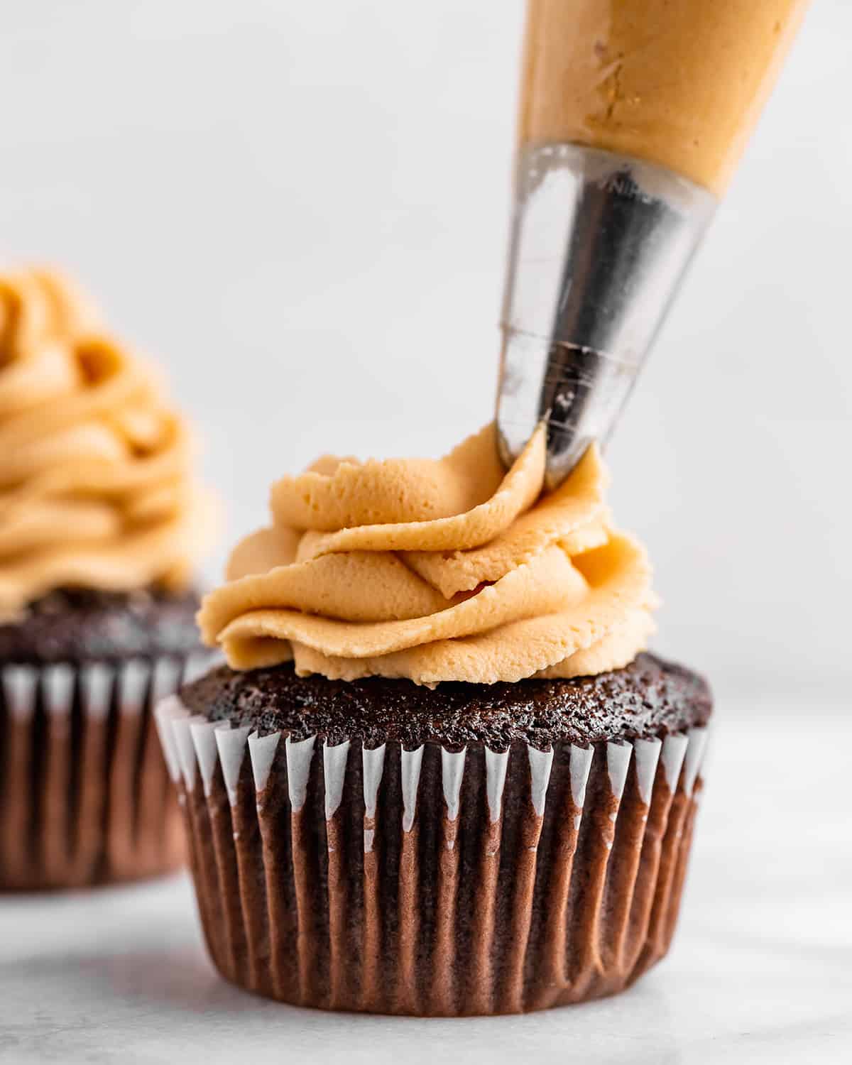 Peanut Butter Frosting being piped on top of a chocolate cupcake