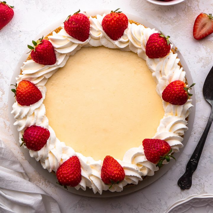 a classic cheesecake decorated with whipped cream and strawberries